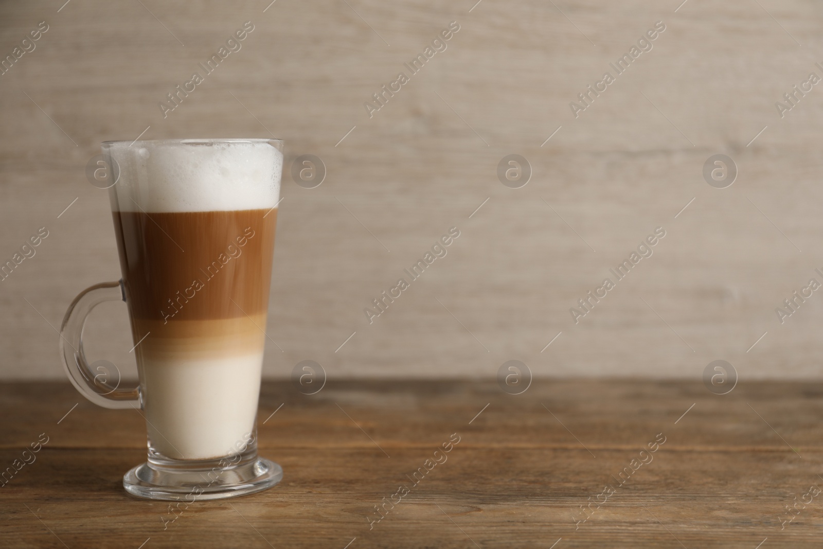 Photo of Hot coffee with milk in glass cup on wooden table. Space for text