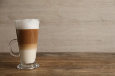 Hot coffee with milk in glass cup on wooden table. Space for text