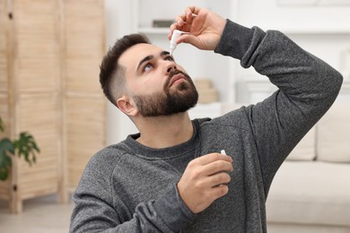 Young man applying medical eye drops indoors