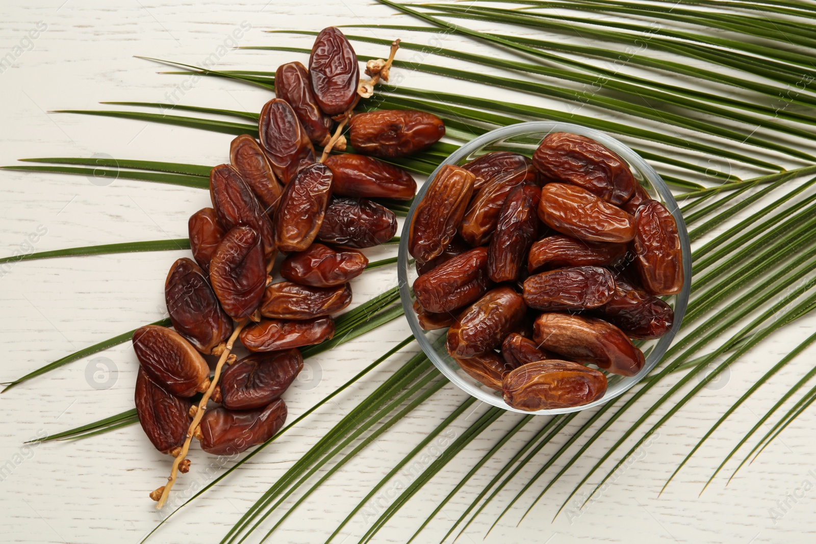 Photo of Tasty sweet dried dates and palm leaf on white wooden table, flat lay