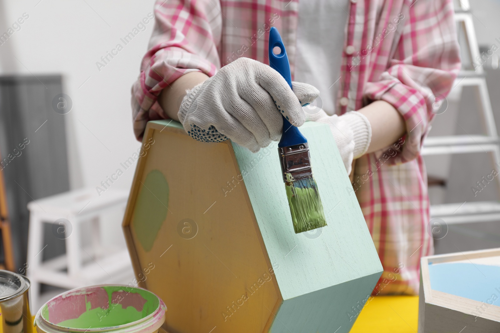 Photo of Woman painting honeycomb shaped shelf with brush indoors, closeup