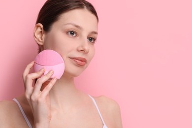 Washing face. Young woman with cleansing brush on pink background, space for text