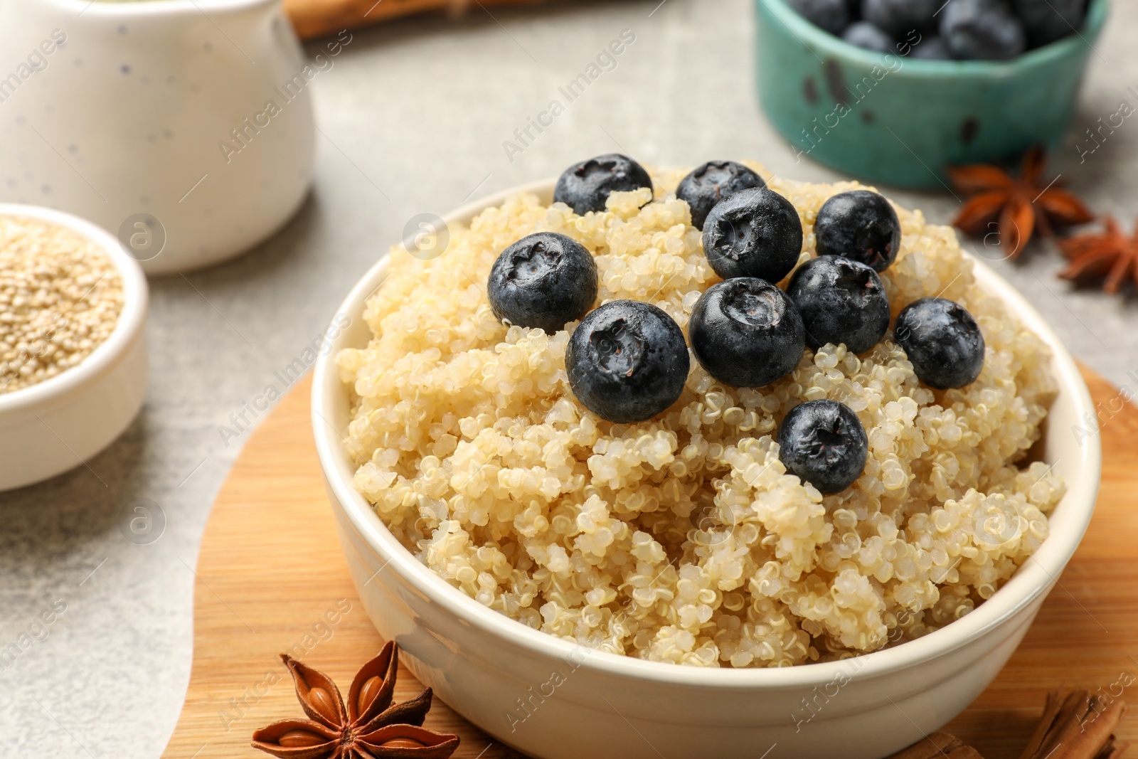 Photo of Tasty quinoa porridge with blueberries in bowl and spices on table, closeup