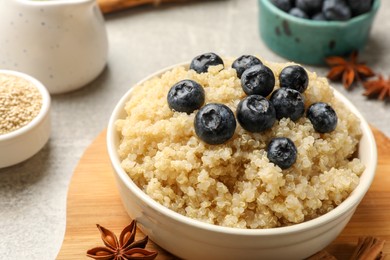 Photo of Tasty quinoa porridge with blueberries in bowl and spices on table, closeup