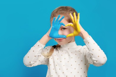 Photo of Little girl making heart with her hands painted in Ukrainian flag colors on light blue background, space for text. Love Ukraine concept