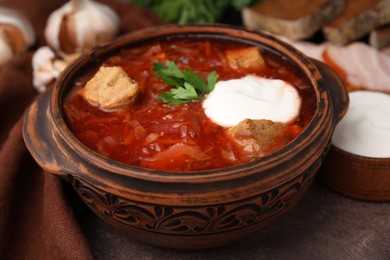 Photo of Tasty borscht with sour cream in bowl on brown textured table, closeup