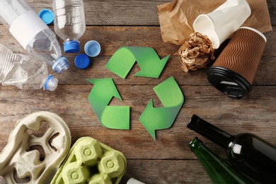 Recycling symbol and different garbage on wooden background, top view