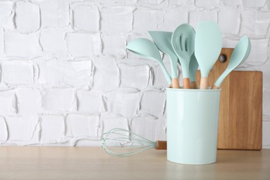 Photo of Holder with different kitchen utensils and cutting board on wooden table. Space for text