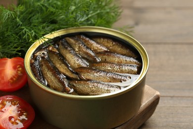 Photo of Tin can with tasty sprats served on wooden table, closeup