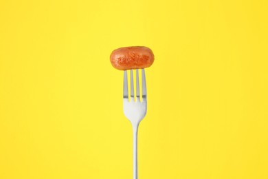 Fork with tasty fried sausage on yellow background
