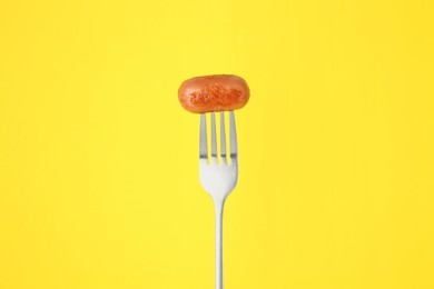 Photo of Fork with tasty fried sausage on yellow background