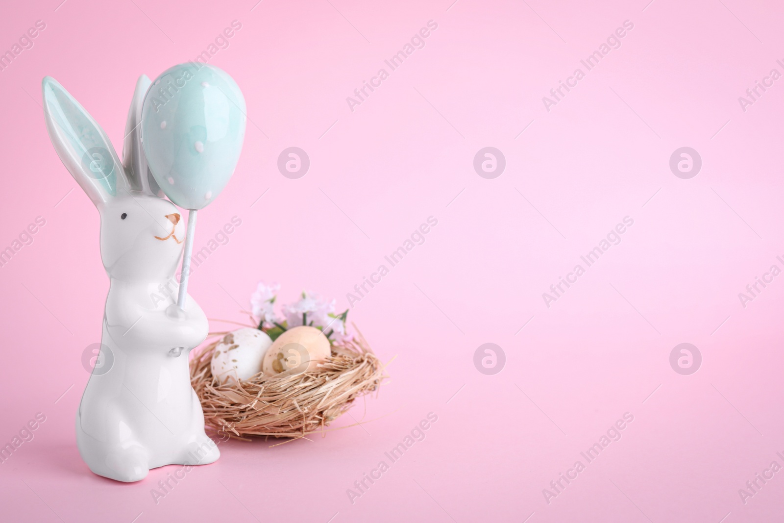 Photo of Easter bunny figure and nest with eggs on pink background. Space for text