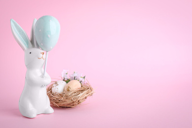 Easter bunny figure and nest with eggs on pink background. Space for text