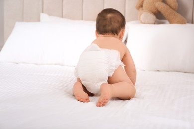 Cute baby in dry soft diaper on white bed at home, back view