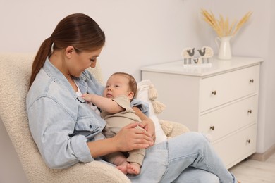 Mother holding her cute newborn baby in armchair at home