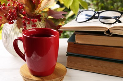 Photo of Cup with hot drink, stack of books and viburnum on white wooden windowsill indoors. Autumn atmosphere