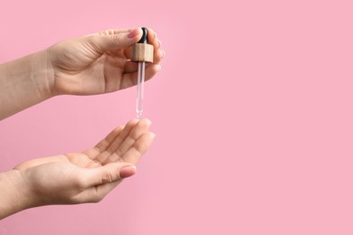 Woman dripping serum from pipette on her hand against pink background, closeup. Space for text