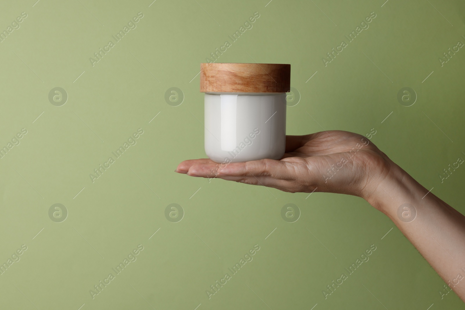 Photo of Woman holding jar of cosmetic product on pale olive background, closeup. Space for text
