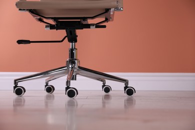 Photo of Modern office chair with wheels on wooden floor, closeup