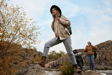 Group of friends with backpacks crossing mountain river on autumn day