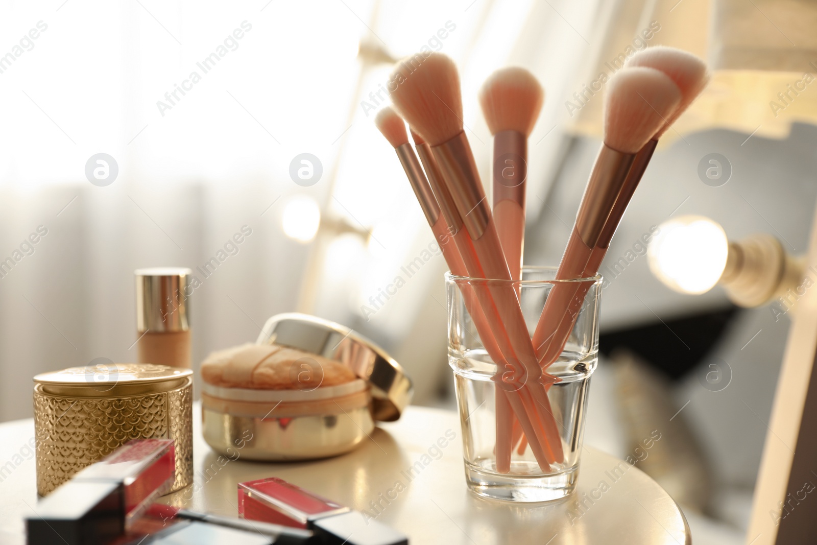 Photo of Makeup products and set of cosmetic brushes on table indoors. Interior element