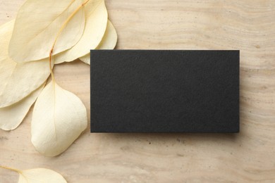 Blank business card and beige leaves on wooden table, flat lay. Mockup for design