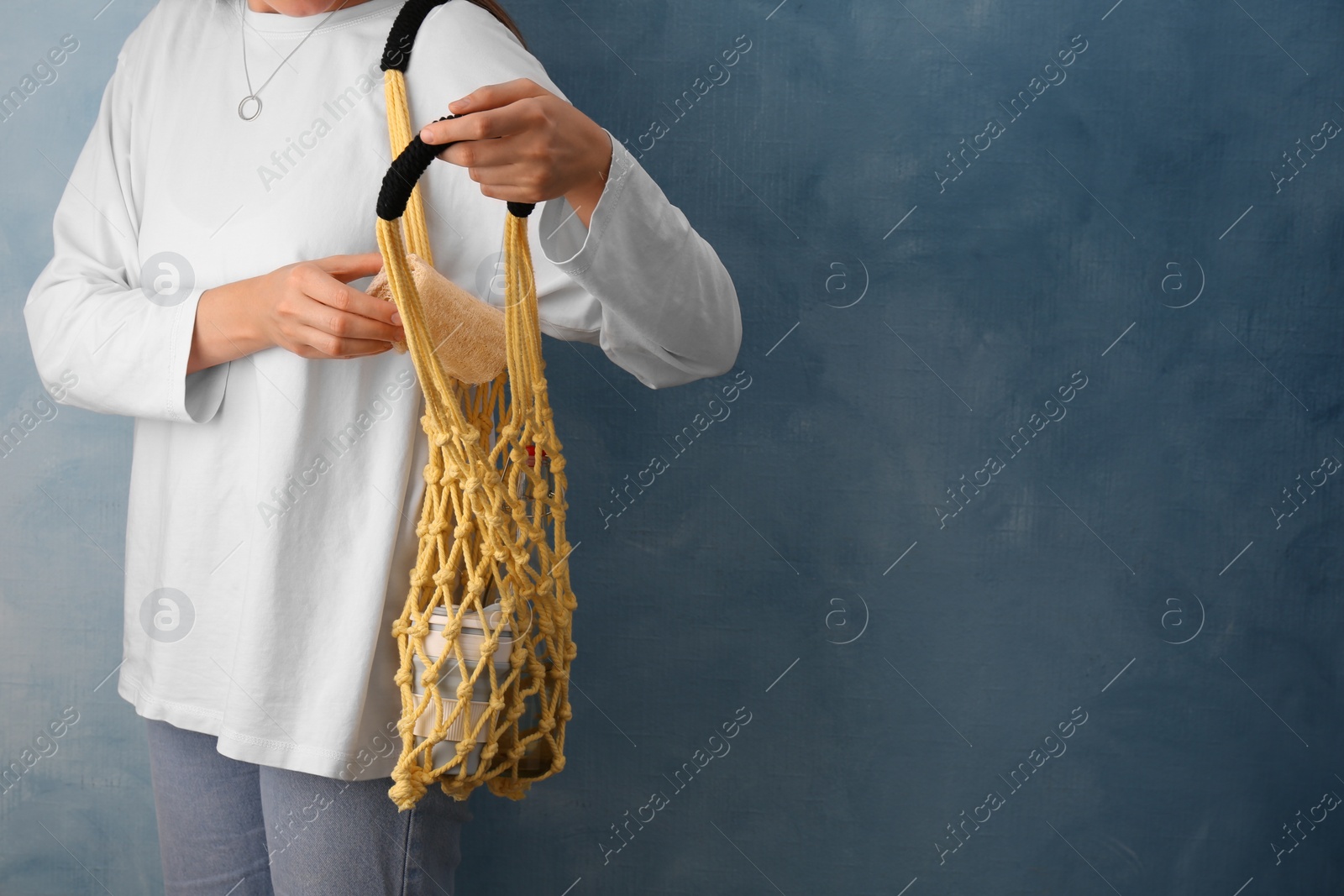 Photo of Woman with net bag full of different items near light blue wall, closeup and space for text. Conscious consumption