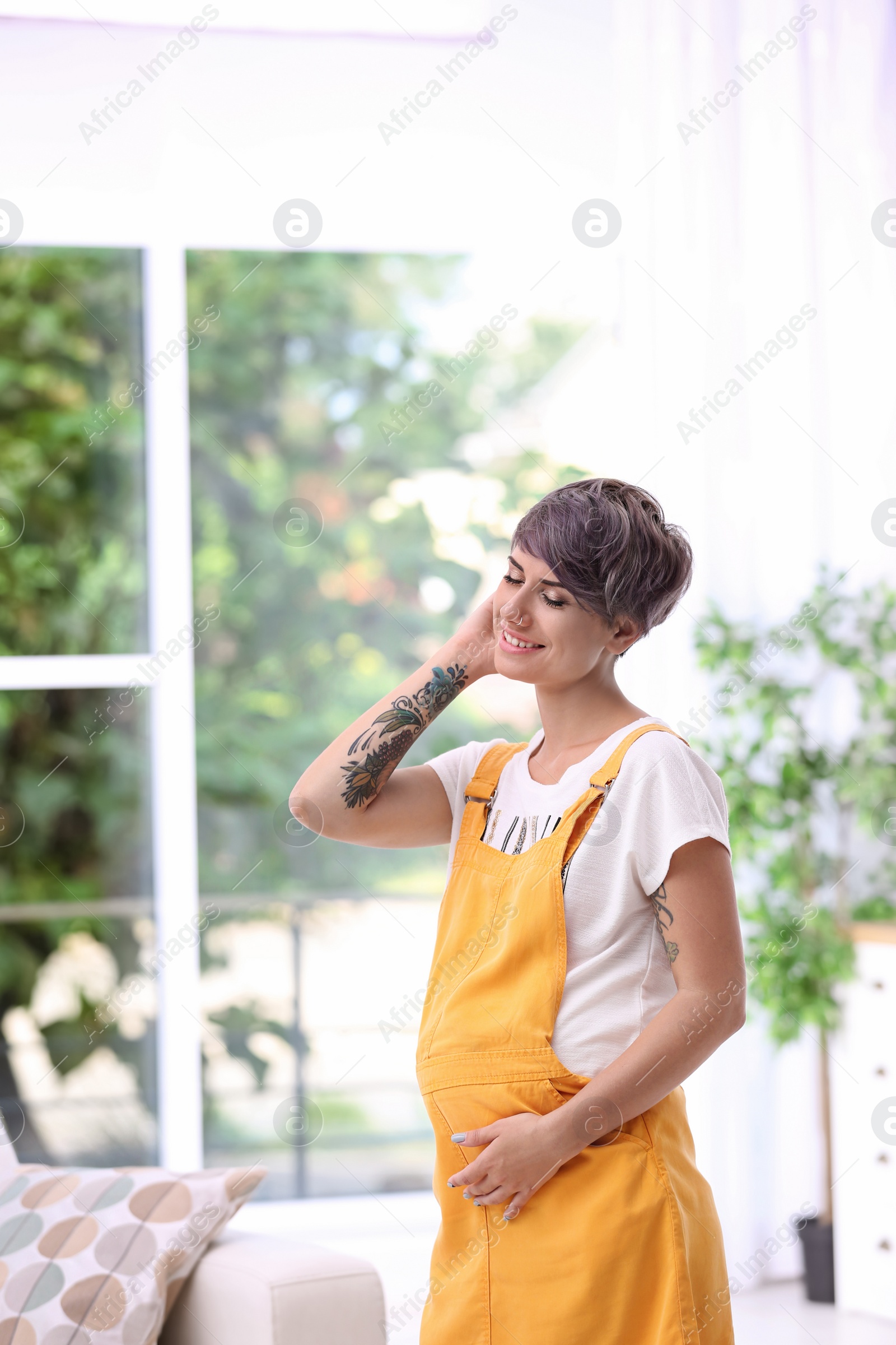 Photo of Trendy pregnant woman with tattoos standing indoors