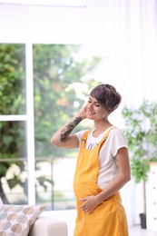 Trendy pregnant woman with tattoos standing indoors