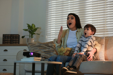 Photo of Emotional young woman and her son watching movie using video projector at home