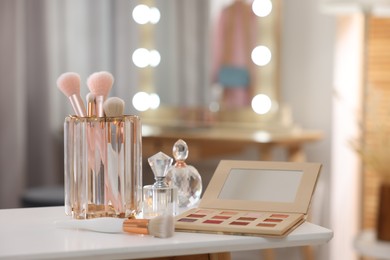 Photo of Set of brushes, eyeshadow palette and perfumes on white table in makeup room