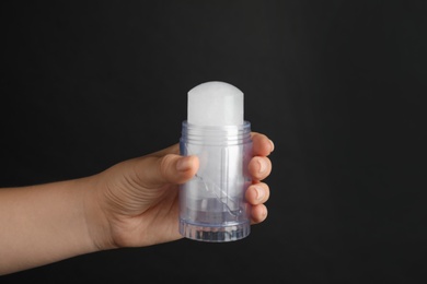 Photo of Young woman holding natural crystal alum deodorant on black background, closeup