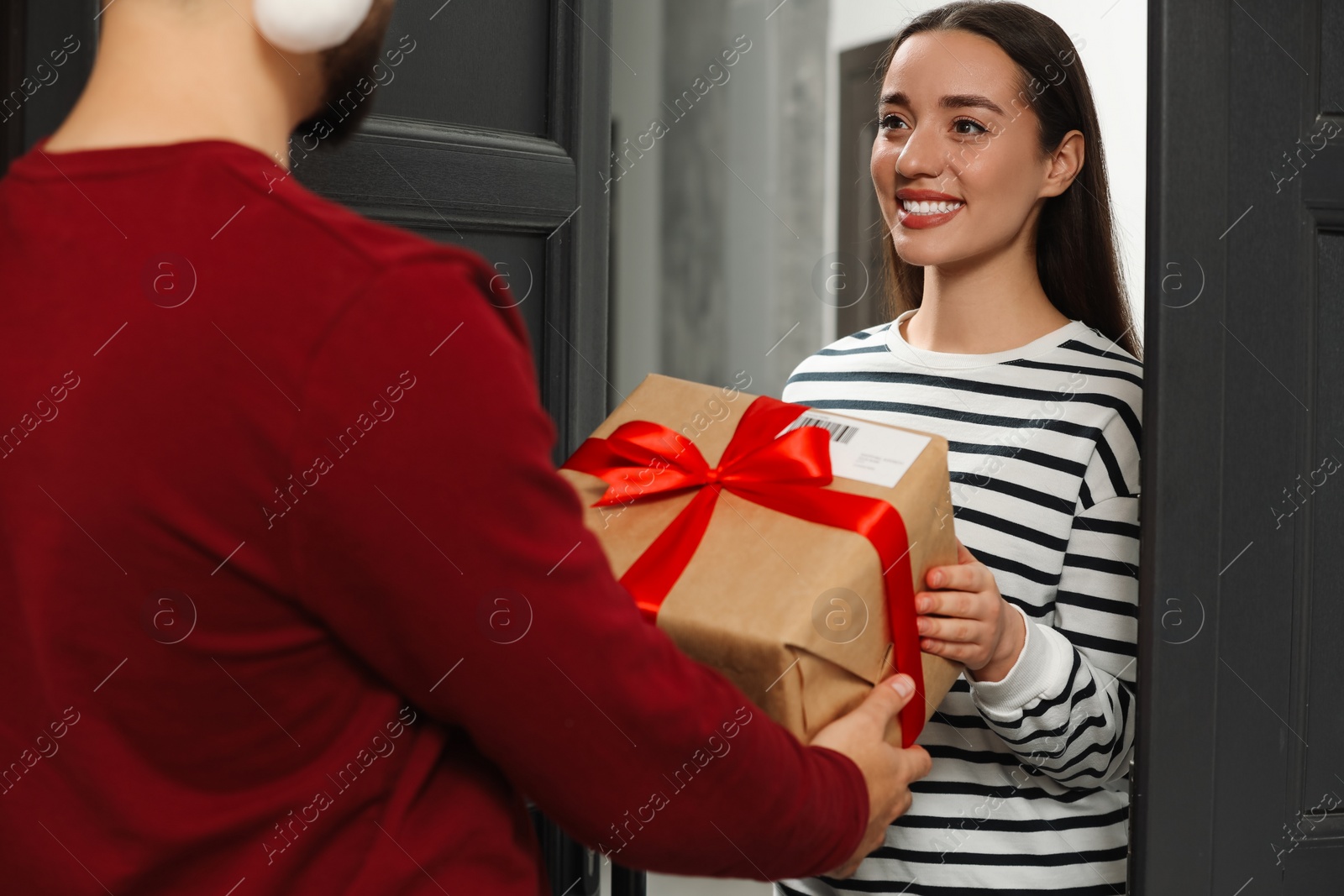 Photo of Courier giving young woman Christmas gift box indoors. Sending present by mail