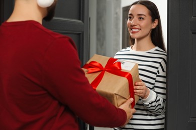 Photo of Courier giving young woman Christmas gift box indoors. Sending present by mail