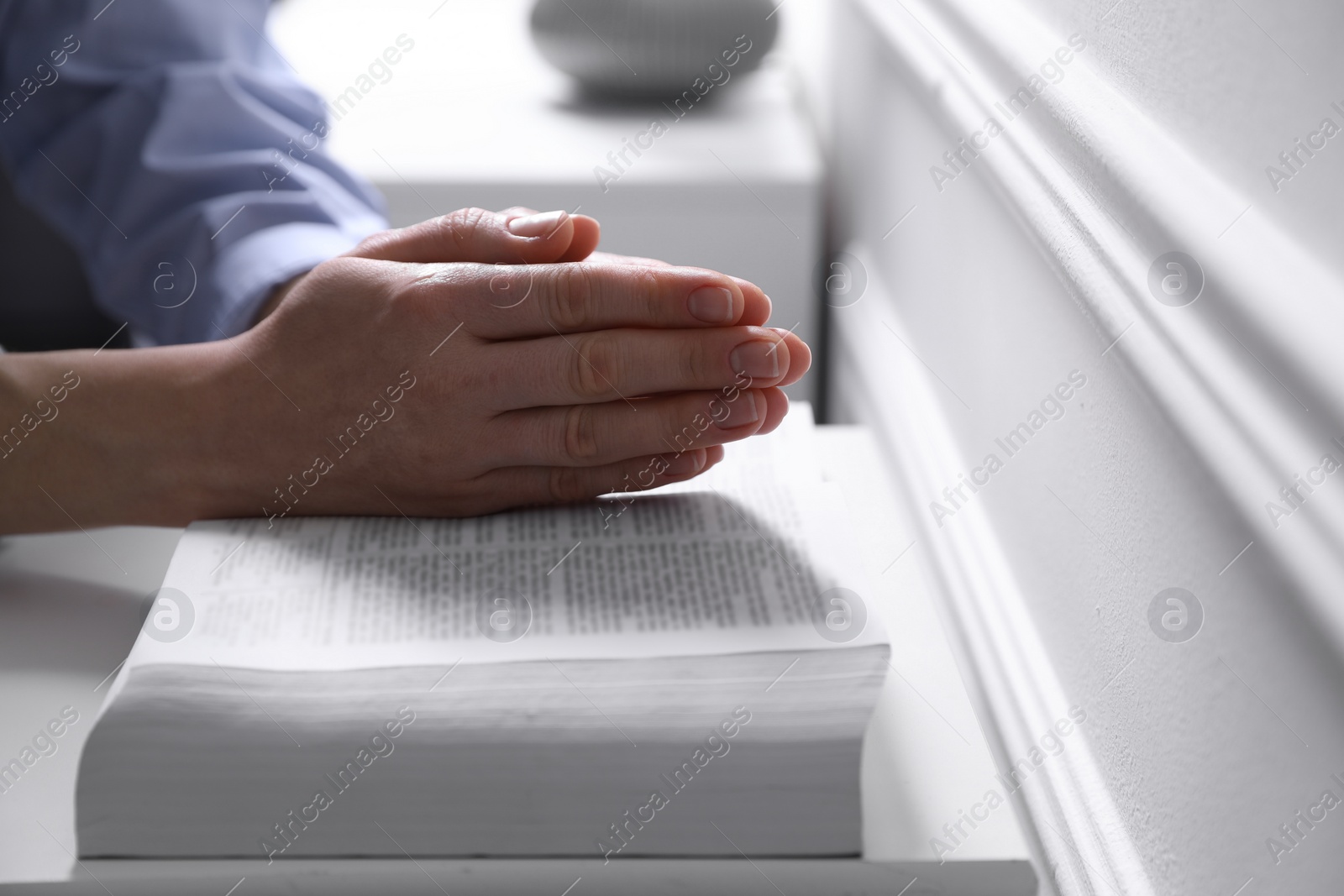 Photo of Religion. Christian woman praying over Bible indoors, closeup