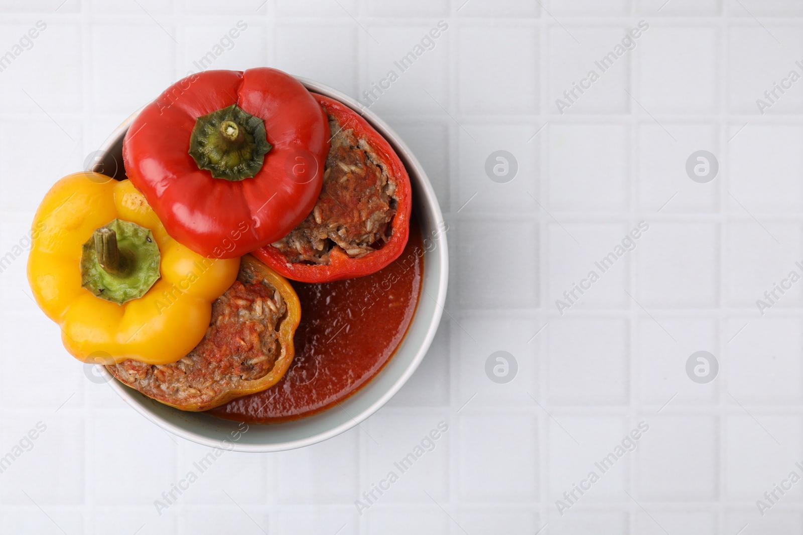 Photo of Delicious stuffed bell peppers on white tiled table, top view. Space for text