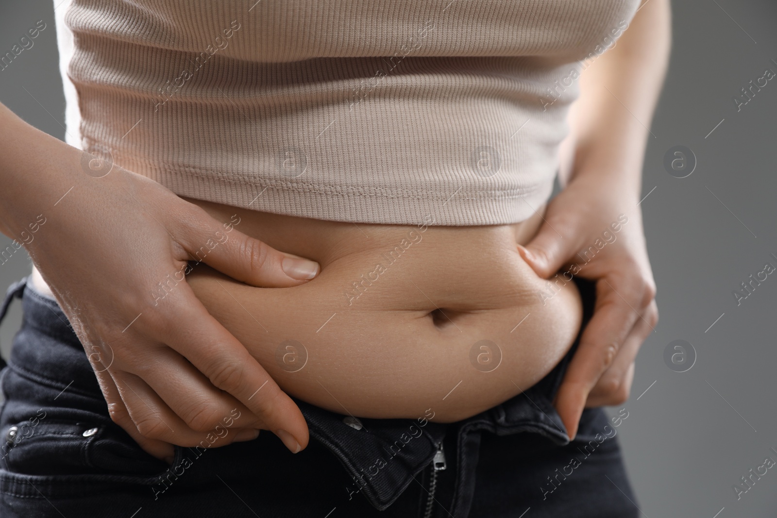 Photo of Woman touching belly fat on grey background, closeup. Overweight problem