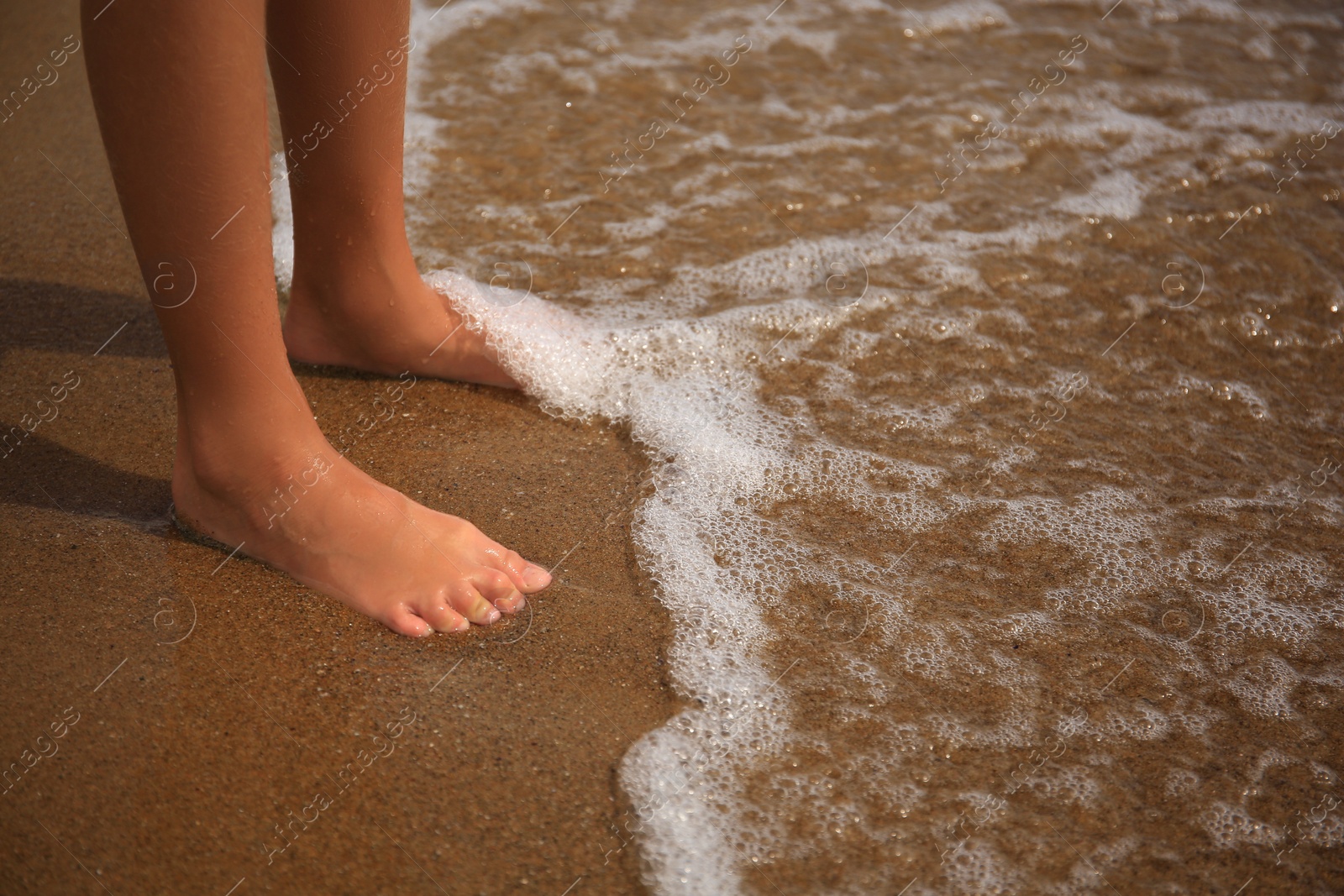 Photo of Little girl standing on sandy beach near sea, closeup. Space for text