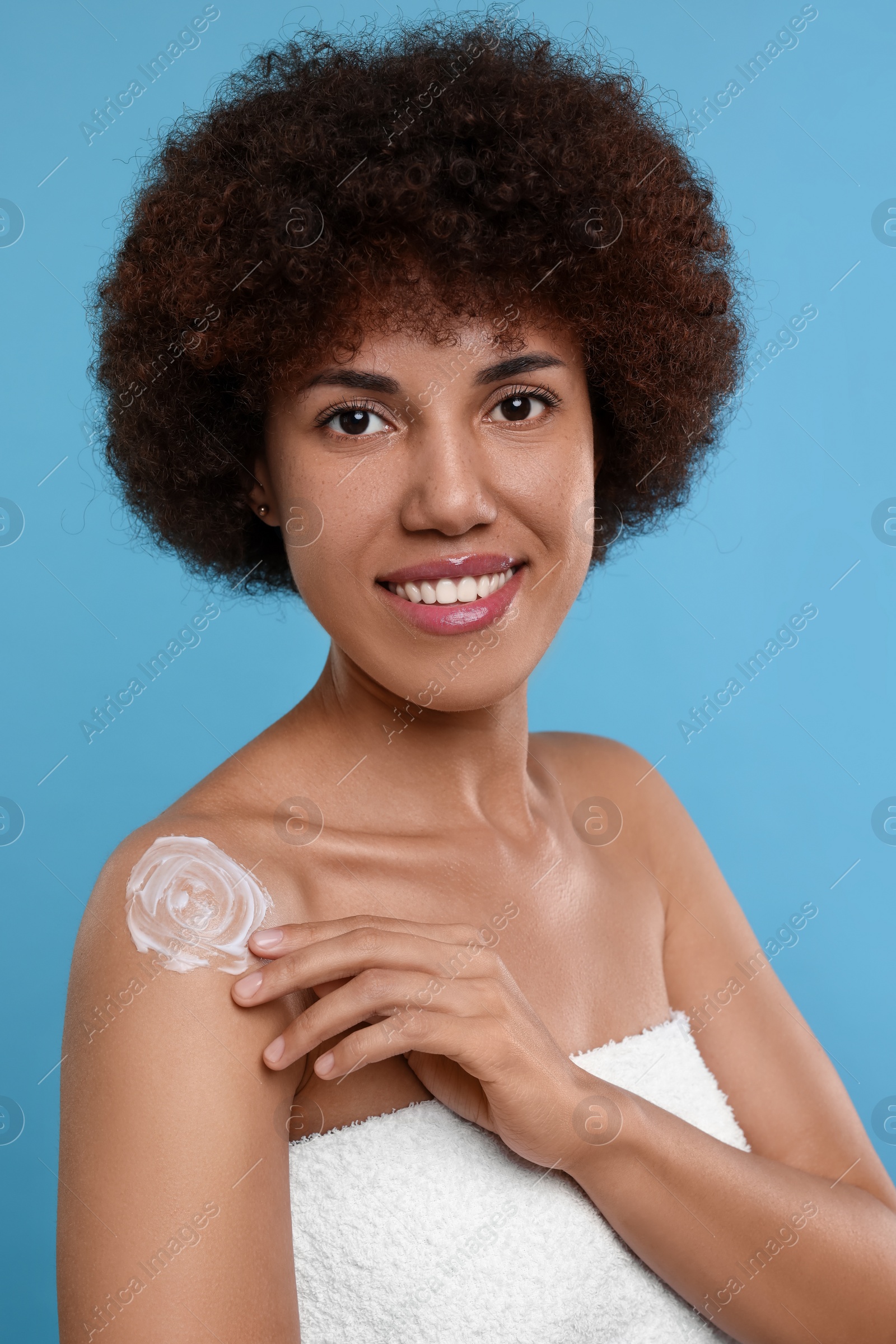 Photo of Beautiful young woman applying body cream onto shoulder on light blue background