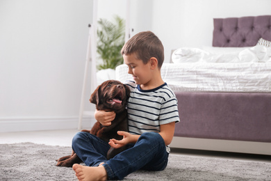 Photo of Little boy with puppy on floor in bedroom. Friendly dog
