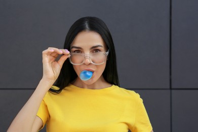 Photo of Beautiful woman blowing gum near dark tiled wall outdoors