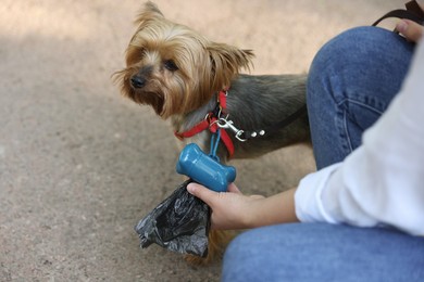 Photo of Woman with cute dog taking waste bag from holder outdoors, closeup