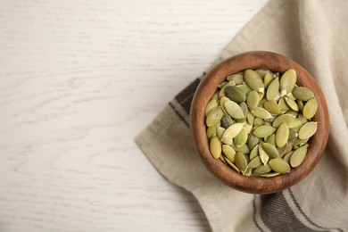 Photo of Bowl of pumpkin seeds with napkin on white wooden table, top view. Space for text