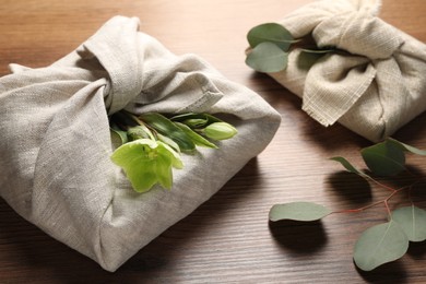 Photo of Furoshiki technique. Gift packed in different fabrics decorated with plants on wooden table