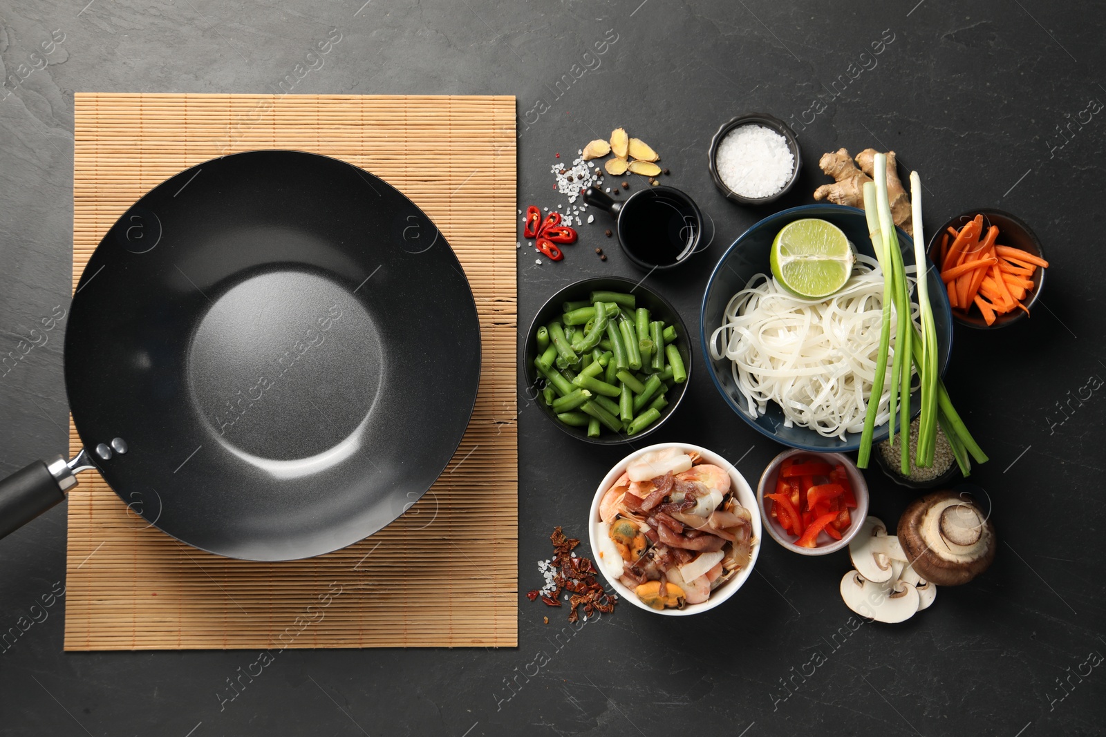 Photo of Flat lay composition with black wok, spices and products on dark textured table