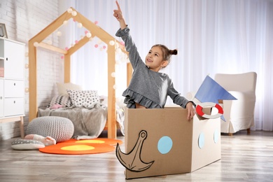 Cute little girl playing with cardboard boat in bedroom