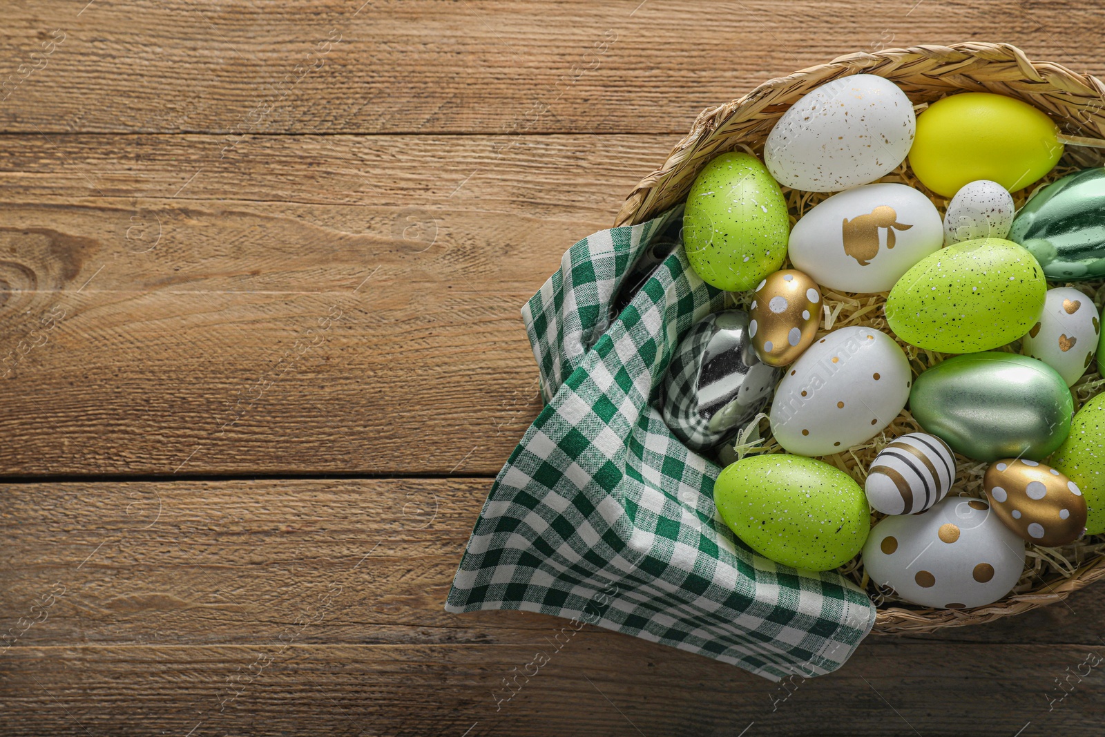 Photo of Many beautifully decorated Easter eggs in wicker basket on wooden table, top view. Space for text