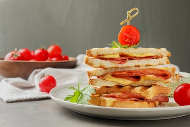 Stack of tasty sandwiches with ham and melted cheese served with tomato on grey textured table, closeup