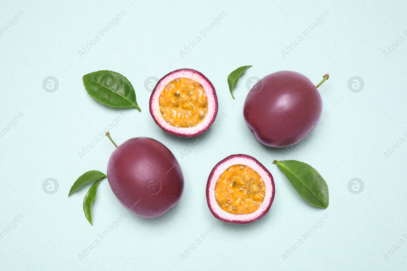 Photo of Fresh ripe passion fruits (maracuyas) with leaves on light background, flat lay