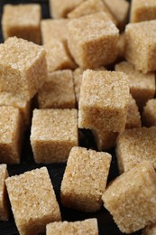 Photo of Brown sugar cubes on dark table, closeup